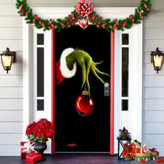 Decorative door with a green hand holding a red ornament, surrounded by Christmas decorations.