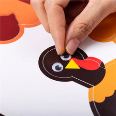 Hand attaching googly eyes to a paper turkey cutout